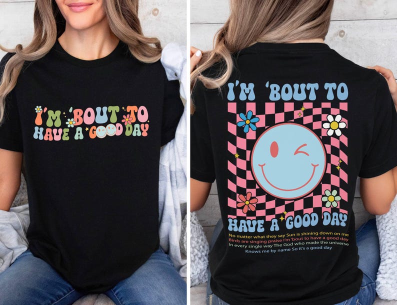 Puede incluir: Camiseta negra con la frase "I'M 'BOUT TO HAVE A GOOD DAY" en letras coloridas de estilo retro. La parte trasera de la camiseta presenta una carita sonriente gui&ntilde;ando un ojo sobre un fondo a cuadros rosa y negro, con texto y flores adicionales.