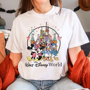 Puede incluir: Camiseta blanca con un gr&aacute;fico colorido de Mickey Mouse, Minnie Mouse, Donald Duck, Goofy y Pluto frente al Castillo de Cenicienta. El texto "Walt Disney World" est&aacute; impreso debajo del gr&aacute;fico.