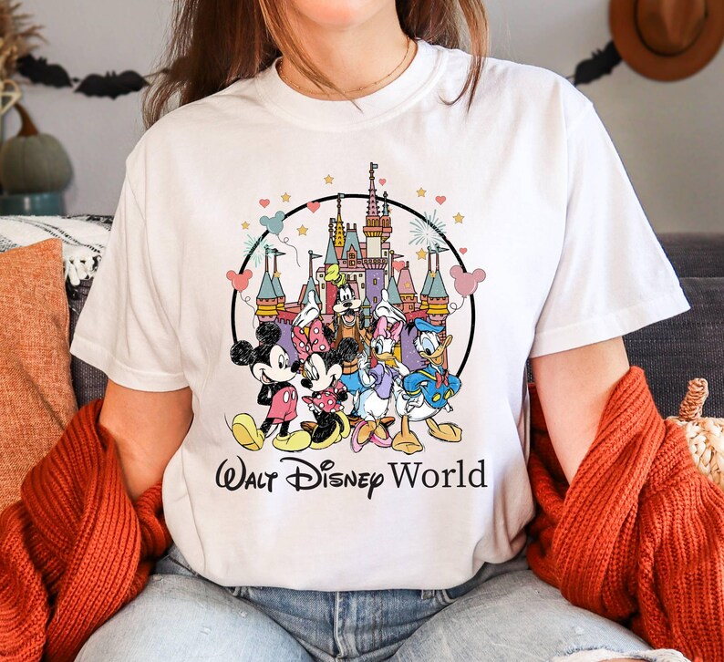 Puede incluir: Camiseta blanca con un gr&aacute;fico colorido de Mickey Mouse, Minnie Mouse, Donald Duck, Goofy y Pluto frente al Castillo de Cenicienta. El texto "Walt Disney World" est&aacute; impreso debajo del gr&aacute;fico.