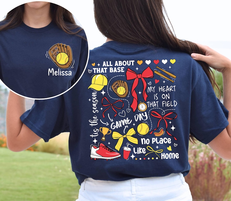 May include: Navy blue t-shirt with a baseball-themed design on the back. The design includes a baseball glove, a baseball, a trophy, a bow, a baseball cap, bats, and the text "tis the season", "ALL ABOUT THAT BASE", "GAME DAY", "MY HEART IS ON THAT FIELD", "no Place Like Home".