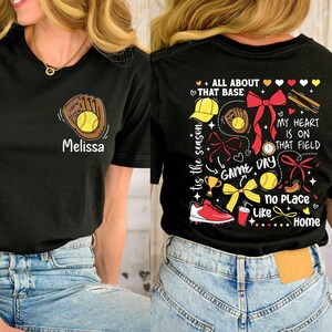 May include: Black t-shirt with a softball design. The front of the shirt has a baseball glove and ball with the name "Melissa". The back of the shirt has a colorful design with the text "'tis the season", "All About That Base", "Game Day", "My Heart Is On That Field", and "No Place Like Home".
