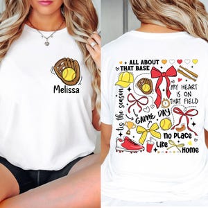 May include: White t-shirt with a softball design on the front and a colorful softball design on the back. The back design includes the text "All About That Base", "Game Day", "My Heart Is On That Field", and "No Place Like Home".