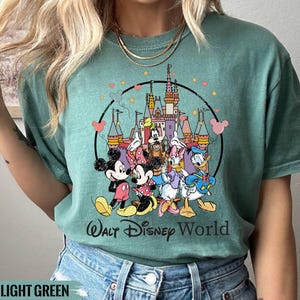 Puede incluir: Una camiseta verde claro con un estampado gr&aacute;fico de Mickey Mouse, Minnie Mouse, Donald Duck, Goofy y Pluto frente al Castillo de Cenicienta. El texto "Walt Disney World" est&aacute; impreso debajo del gr&aacute;fico.
