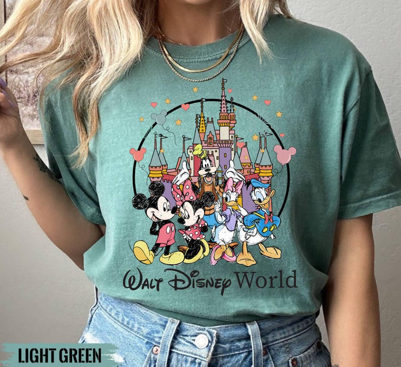 Puede incluir: Una camiseta verde claro con un estampado gr&aacute;fico de Mickey Mouse, Minnie Mouse, Donald Duck, Goofy y Pluto frente al Castillo de Cenicienta. El texto "Walt Disney World" est&aacute; impreso debajo del gr&aacute;fico.
