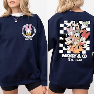 Puede incluir: Sudadera azul marino con un patr&oacute;n a cuadros y un gr&aacute;fico de Mickey Mouse y sus amigos en la espalda. La parte delantera de la sudadera tiene un gr&aacute;fico de Daisy Duck con la palabra "Sister" debajo.