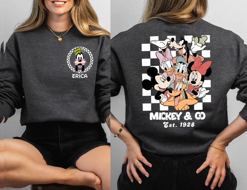 Puede incluir: Una sudadera gris con un patr&oacute;n a cuadros y un gr&aacute;fico de Mickey Mouse y sus amigos. El texto "Mickey & Co. Est. 1928" est&aacute; impreso debajo del gr&aacute;fico. La sudadera tiene un bolsillo en el lado izquierdo con un gr&aacute;fico de Goofy y el nombre "Erica" impreso debajo.