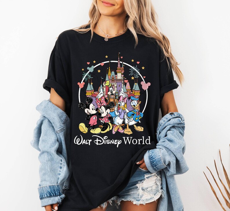 Puede incluir: Camiseta negra con un gr&aacute;fico colorido de Mickey Mouse, Minnie Mouse, Donald Duck, Goofy y Pluto frente al Castillo de Cenicienta. El texto "Walt Disney World" est&aacute; impreso debajo del gr&aacute;fico.