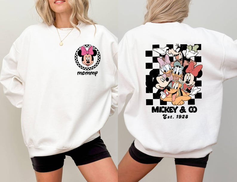 Puede incluir: Sudadera blanca con un patr&oacute;n de cuadros blanco y negro y un grupo de personajes de Disney que incluyen a Mickey Mouse, Minnie Mouse, Donald Duck, Goofy y Pluto. El texto "Mickey & Co. Est. 1928" est&aacute; impreso debajo de los personajes. La parte delantera de la sudadera tiene una imagen en blanco y negro de Minnie Mouse con la palabra "mam&aacute;" impresa debajo.