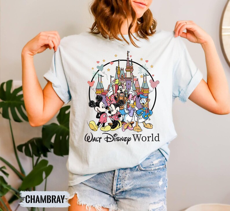 Puede incluir: Una camiseta azul claro con una ilustraci&oacute;n de estilo vintage de Mickey Mouse, Minnie Mouse, Donald Duck, Goofy y Pluto frente al Castillo de Cenicienta. El texto "Walt Disney World" est&aacute; impreso debajo de la ilustraci&oacute;n.