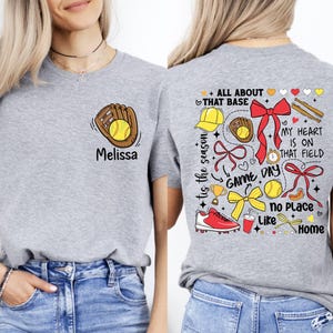 May include: Gray t-shirt with a softball design on the front and a colorful softball design on the back. The back design includes the text "All About That Base", "Game Day", "My Heart Is On That Field", "No Place Like Home", and "Tis The Season".