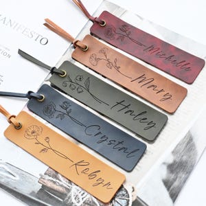 May include: Five leather bookmarks in different colours, each with a floral design and a name. The bookmarks have a leather strap and a metal eyelet. The names are Michelle, Mary, Haley, Crystal, and Robyn.