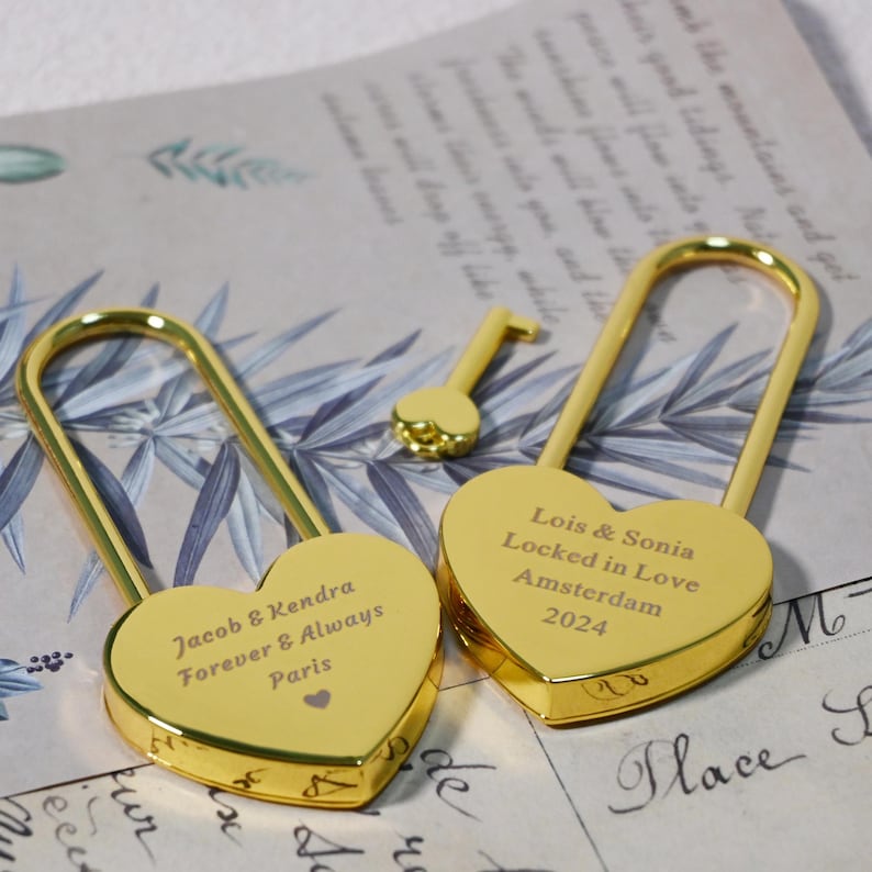 May include: Two gold heart-shaped padlocks with keys. One padlock says "Jacob & Kendra Forever & Always Paris" and the other says "Lois & Sonia Locked in Love Amsterdam 2024".