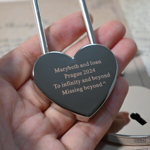 May include: Silver heart-shaped padlock with an inscription that reads "Marybeth and Ioan Prague 2024 To infinity and beyond Missing beyond ^".
