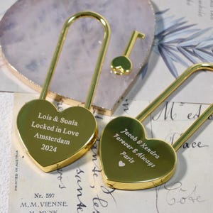 May include: Two gold heart-shaped padlocks with keys. The padlocks are engraved with personalised messages: "Lois & Sonia Locked in Love Amsterdam 2024" and "Jacob & Kendra Forever & Always Paris".