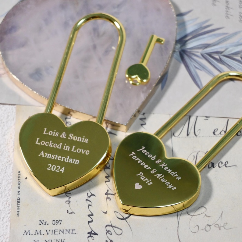 May include: Two gold heart-shaped padlocks with keys. The padlocks are engraved with personalized messages: "Lois & Sonia Locked in Love Amsterdam 2024" and "Jacob & Kendra Forever & Always Paris".