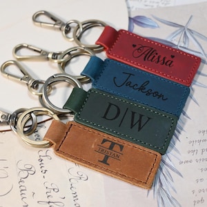 Puede incluir: Cinco llaveros de cuero con diferentes grabados personalizados. Los llaveros son de varios colores, incluyendo rojo, azul, verde y marrón. Los grabados incluyen nombres, iniciales y un monograma.