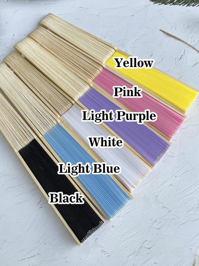 May include: A set of seven hand fans in various colors, including black, light blue, white, light purple, pink, yellow, and natural wood. The fans are arranged in a row, with the black fan at the bottom and the natural wood fan at the top.