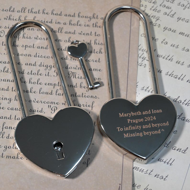 May include: Two silver heart-shaped padlocks with a key. The padlock on the right has the inscription "Marybeth and Ioan Prague 2024 To infinity and beyond Missing beyond^"