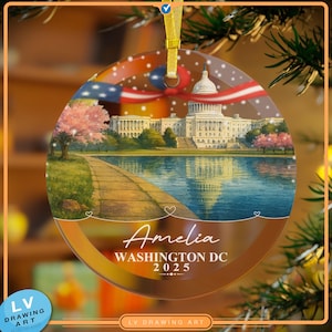 Peut inclure: Un ornement rond, plat et transparent présentant une illustration imprimée du Capitole des États-Unis, d'un bassin réfléchissant et de cerisiers en fleurs. Le texte indique Amelia, WASHINGTON DC et 2025. Il est suspendu par un ruban doré.