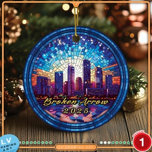May include: A round, blue Christmas ornament featuring a cityscape design with the text "Broken Arrow 2025." The ornament has a gold string for hanging and a mosaic-style background with a sunset.
