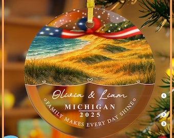 Könnte beinhalten: Ein rundes, flaches, transparentes Ornament mit einer Strandlandschaft mit Dünen und Meereswellen. Ein rot-weiß-blaues Band ist oben befestigt. Der Text lautet: Olivia & Liam, MICHIGAN, 2025, FAMILY MAKES EVERY DAY SHINE.