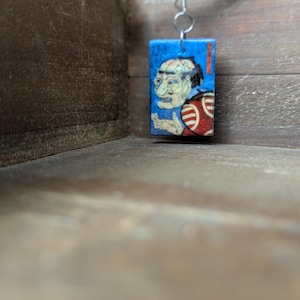 以下が含まれることがあります： 男性の顔のヴィンテージな日本の木版画が描かれた、長方形の青と赤のタイルが付いたイヤリングのペアです。