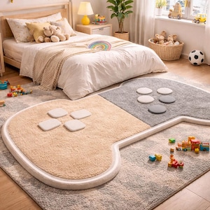 Könnte beinhalten: Ein beigefarbener und grauer Teppich in Form eines Videospiel-Controllers. Der Teppich hat einen weißen Rand und verfügt über vier quadratische Tasten und sechs runde Tasten. Der Teppich befindet sich in einem Schlafzimmer mit Bett und Spielzeug.