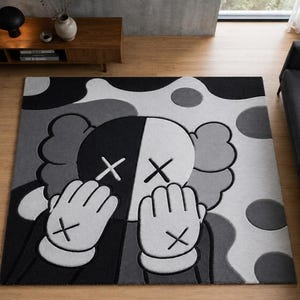 Pu&ograve; includere: Un tappeto rettangolare con un design grafico nero, bianco e grigio che raffigura un personaggio dei cartoni animati con occhi a forma di X e mani che coprono il viso. Il motivo di sfondo &egrave; composto da grandi forme arrotondate e cerchi.