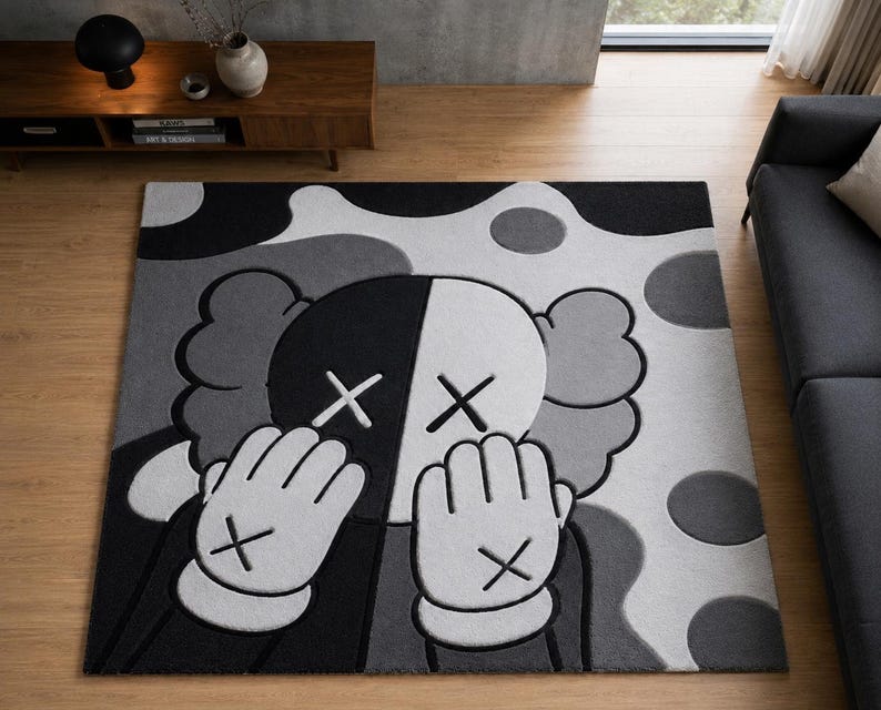 Pu&ograve; includere: Un tappeto rettangolare con un design grafico nero, bianco e grigio che raffigura un personaggio dei cartoni animati con occhi a forma di X e mani che coprono il viso. Il motivo di sfondo &egrave; composto da grandi forme arrotondate e cerchi.