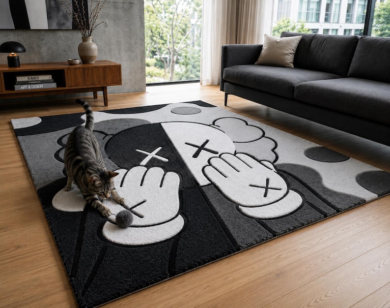 Pu&ograve; includere: Un tappeto rettangolare con un design grafico nero, bianco e grigio raffigurante due mani in stile cartone animato con occhi a forma di X e dita che coprono il volto. Il tappeto ha una superficie testurizzata su un pavimento in legno chiaro.