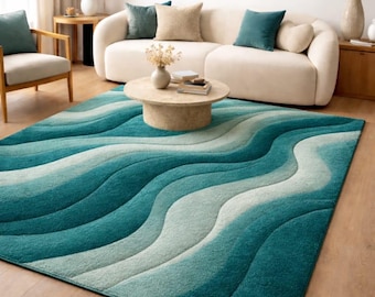 May include: A teal and blue area rug with a wave pattern. The rug is in a living room setting with a white sofa, wooden furniture, and a round coffee table. The rug's design features flowing, curved lines in varying shades of blue and teal.