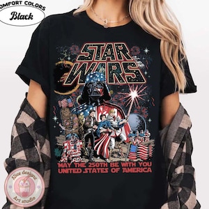 Op de afbeelding: Zwart T-shirt met een Star Wars-afbeelding met Darth Vader in een Amerikaans vlagontwerp. Het shirt bevat de tekst "MAY THE 250TH BE WITH YOU UNITED STATES OF AMERICA". Het shirt heeft ook de woorden "COMFORT COLORS" en "Black" erop gedrukt.