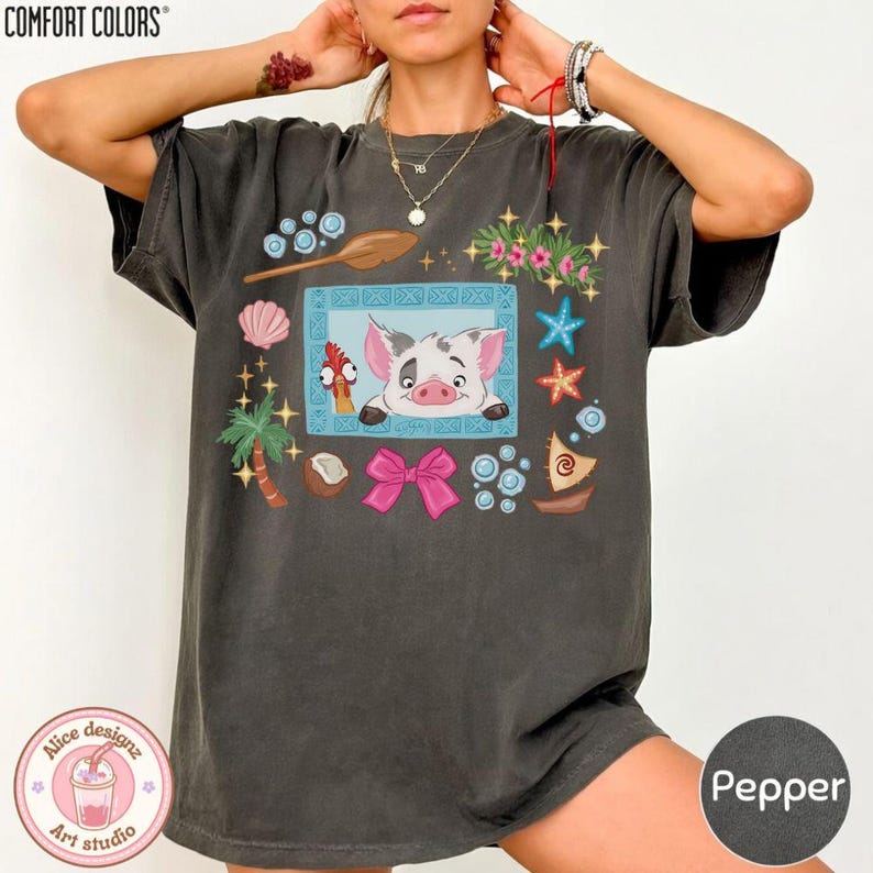 Puede incluir: Camiseta Comfort Colors color pimienta con una ilustraci&oacute;n de dibujos animados de un cerdo y un gallo en un marco azul, rodeada de elementos tropicales. La camiseta tambi&eacute;n tiene el texto "Alice designz art studio".