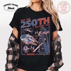 May include: Black Comfort Colors t-shirt with a graphic featuring Darth Vader, spaceships, and fireworks in red, white, and blue. The text reads "May the 250th Be With You" and "NAME:" at the bottom.