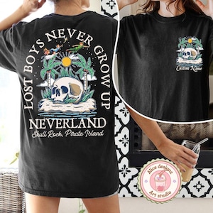 May include: Black t-shirt with a graphic print of a skull on an island with palm trees and the text "Lost Boys Never Grow Up Neverland Skull Rock, Pirate Island".