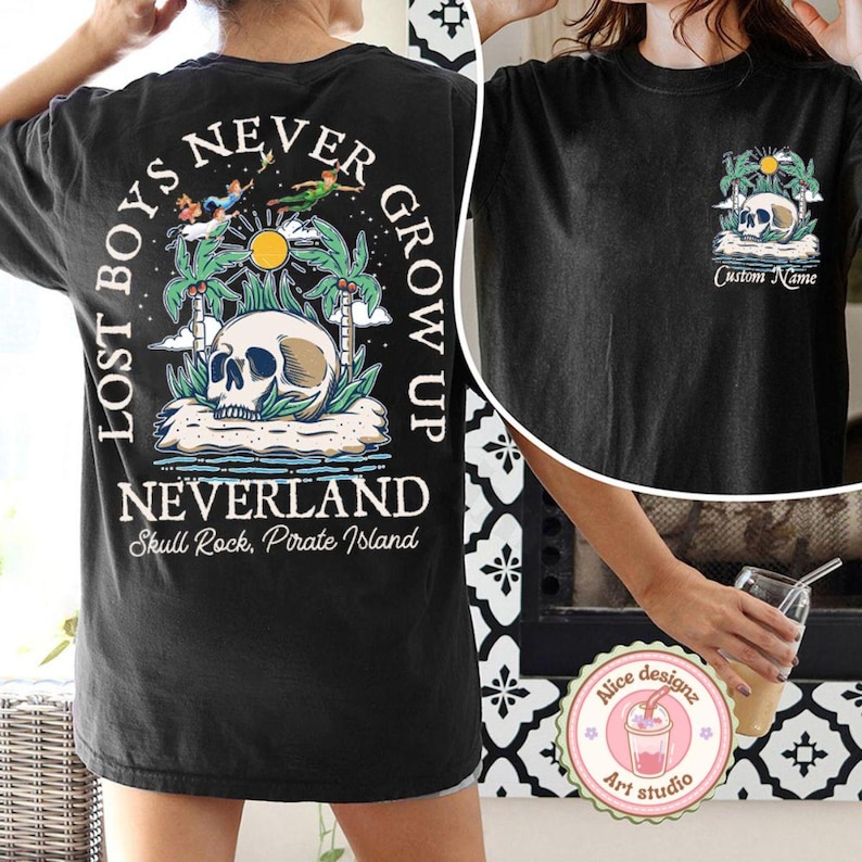 May include: Black t-shirt with a graphic print of a skull on an island with palm trees and the text "Lost Boys Never Grow Up Neverland Skull Rock, Pirate Island".
