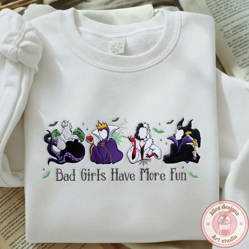 May include: White sweatshirt featuring embroidered cartoon villains with the text "Bad Girls Have More Fun." The design includes Ursula, the Evil Queen, Cruella de Vil, and Maleficent. The design is in shades of purple, black, white, and green.