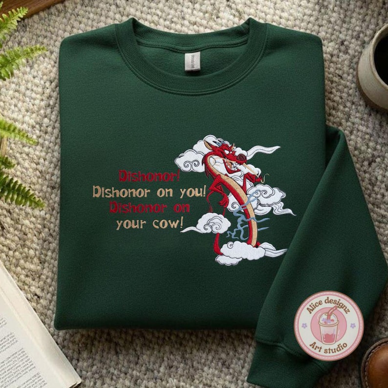 May include: A dark green sweatshirt featuring an embroidered design of a red dragon amidst white clouds. The text "Dishonor on you! Dishonor on your cow!" is embroidered in red and tan. A small logo is visible on the sleeve.