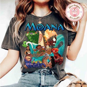 Puede incluir: Una camiseta gris con un estampado gr&aacute;fico de personajes de la pel&iacute;cula animada Moana. El gr&aacute;fico incluye a Moana, Maui y otros personajes de la pel&iacute;cula. El texto "Moana" est&aacute; impreso en letras grandes en la camiseta.