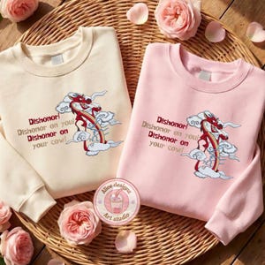 May include: Two crewneck sweatshirts, one cream and one pink, with a red dragon design and the text "Dishonor! Dishonor on you! Dishonor on your cow!" A round sticker with a drink graphic is also visible.