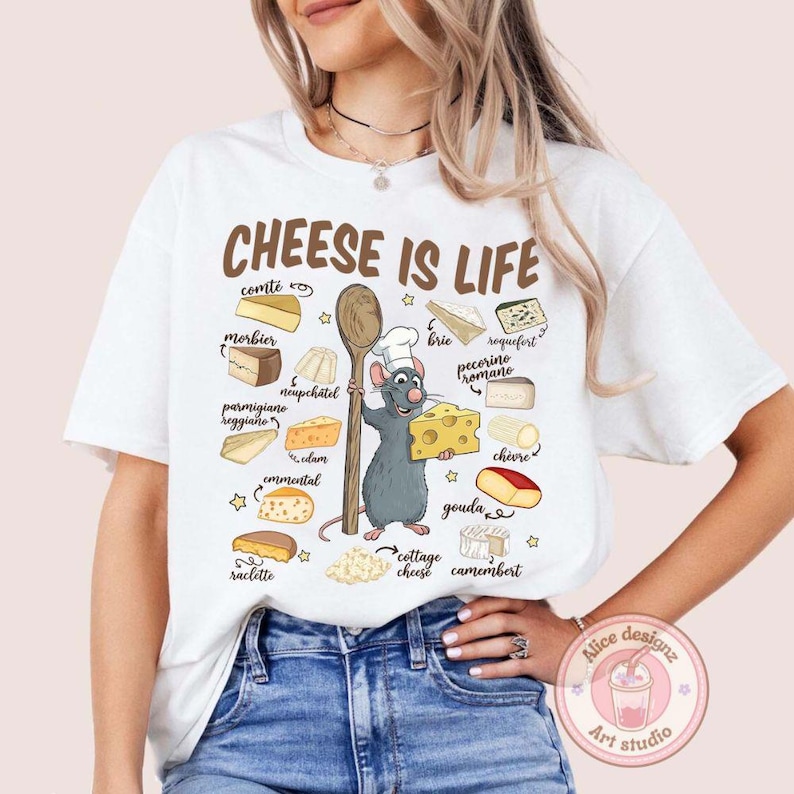 Puede incluir: Camiseta blanca con la frase "CHEESE IS LIFE" e ilustraciones de quesos. Un chef rata de dibujos animados sostiene una cuchara de madera y un bloque de queso. Las variedades de queso incluyen Gouda, Brie y Camembert.