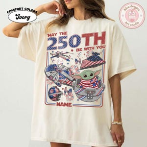 May include: Ivory Comfort Colors t-shirt with a patriotic design. The graphic features a Star Wars theme with the text "MAY THE 250TH BE WITH YOU" and a Baby Yoda character. The design incorporates American flag elements.