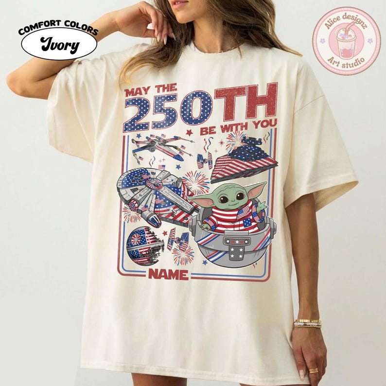 May include: Ivory Comfort Colors t-shirt with a patriotic design. The graphic features a Star Wars theme with the text "MAY THE 250TH BE WITH YOU" and a Baby Yoda character. The design incorporates American flag elements.