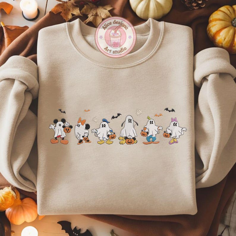 K&ouml;nnte beinhalten: Beiges Sweatshirt mit Rundhalsausschnitt und Halloween-Motiv. Das Design zeigt Cartoon-Geister, die als beliebte Charaktere verkleidet sind und jeweils einen K&uuml;rbis-Eimer halten. Das Sweatshirt hat einen runden Ausschnitt und lange &Auml;rmel.
