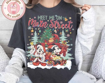 May include: A black t-shirt with a Christmas-themed design featuring Mickey and Minnie Mouse. The design includes a Christmas tree, presents, and the text "Meet Me On Main Street".