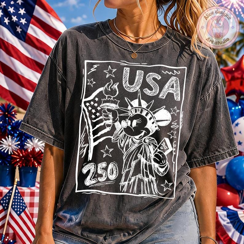 May include: Dark gray t-shirt featuring a white graphic of the Statue of Liberty with Mickey Mouse's face, holding a torch and a scroll that says "July". The word "USA" is above the image, and the number "250" is below. The shirt has a vintage, faded look.