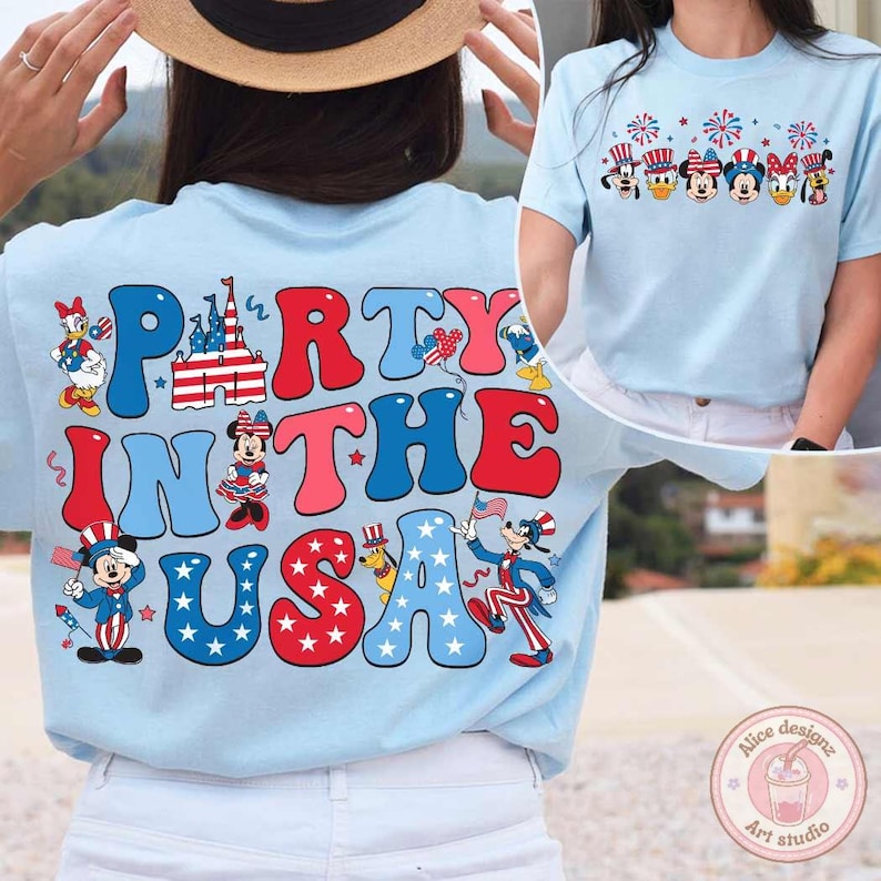 Peut inclure: T-shirt bleu clair avec l'inscription "Party in the USA" en rouge, blanc et bleu. Le t-shirt pr&eacute;sente des personnages de dessins anim&eacute;s et des images patriotiques, notamment des feux d'artifice et le drapeau am&eacute;ricain. Un deuxi&egrave;me t-shirt est visible avec un design similaire.