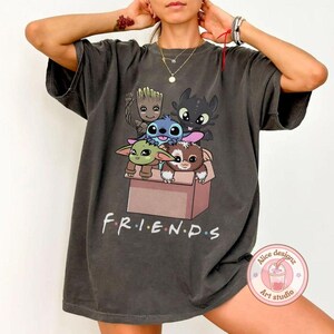 Peut inclure: T-shirt gris fonc&eacute; avec un motif de personnages de dessins anim&eacute;s dans une bo&icirc;te. Le mot "FRIENDS" est imprim&eacute; en blanc en dessous. Le t-shirt a des manches courtes et un col rond. Le tissu est doux.