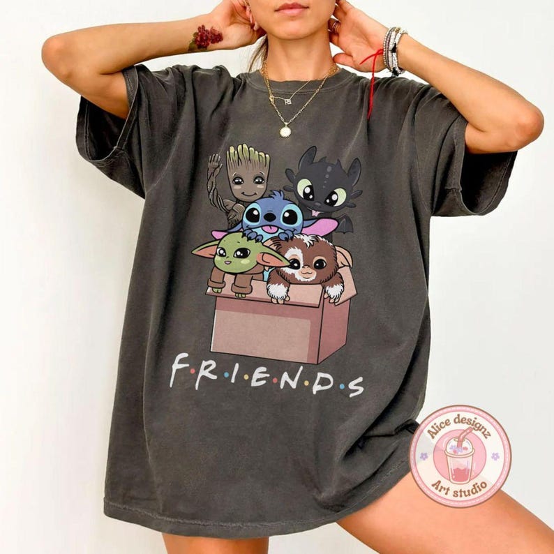 Peut inclure: T-shirt gris fonc&eacute; avec un motif de personnages de dessins anim&eacute;s dans une bo&icirc;te. Le mot "FRIENDS" est imprim&eacute; en blanc en dessous. Le t-shirt a des manches courtes et un col rond. Le tissu est doux.