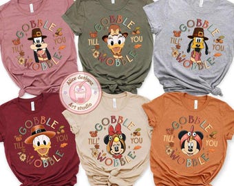 May include: A collection of six short-sleeved t-shirts in various colors, each featuring a Thanksgiving-themed design. The shirts display cartoon characters in pilgrim hats with the text "Gobble Till You Wobble" in a circular design.